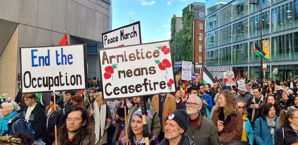 Photo of a demonstration with people holding up a sign saying 'Armistice means ceasefire'